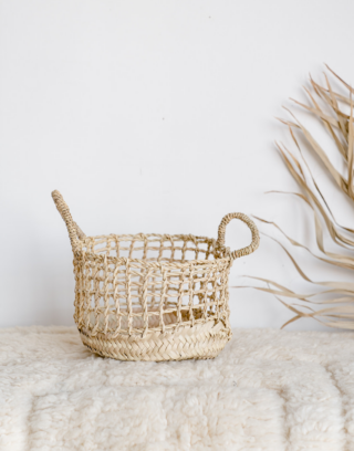 Petit panier en paille au tressage ajouré dans un décor bohème, posé sur un tapis