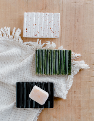 Notre trio de porte-savon en argile émaillée posé sur une table en bois avec un carré d'ambre et une serviette en lin blanche