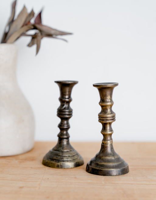 Deux mini bougeoirs en laiton posés sur une table en bois près d'un vase blanc