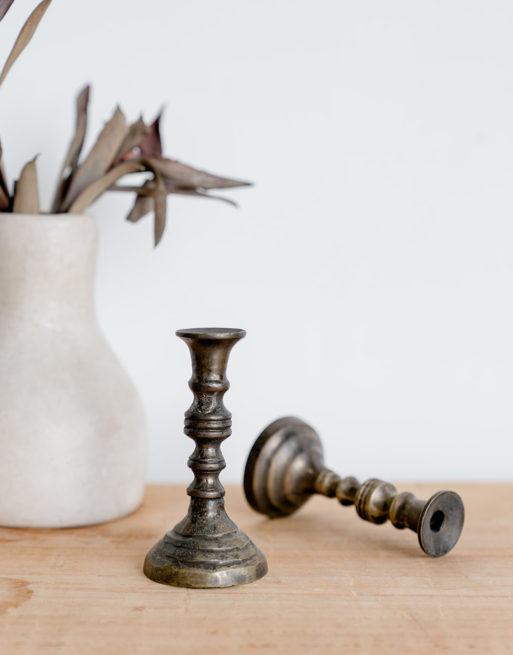 Notre mini bougeoir en laiton posé sur une table en bois près d'un autre bougeoir et d'un vase blanc