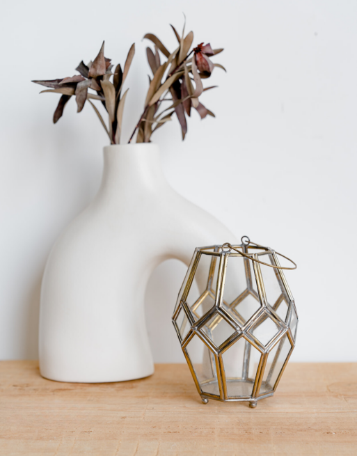 Notre photophore à poser en laiton doré sur une table près d'un joli vase blanc agrémenté de feuilles séchées