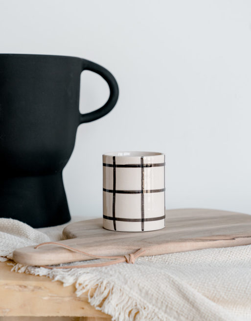 Notre tasse ronde à carreaux posée sur une planche en noyer près d'un plaid écru et d'un vase noir