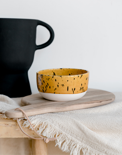 Notre bol tacheté jaune posé sur une table en bois et une planche en noyer près d'un vase noir