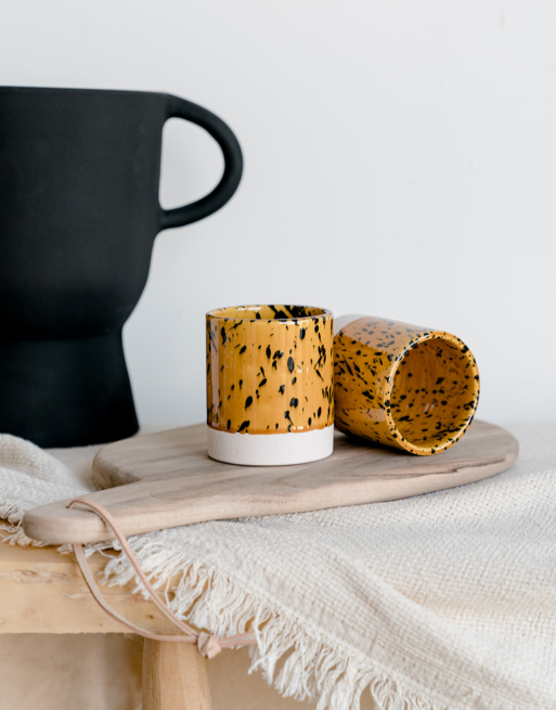 Notre tasse tachetée jaune posée sur une table en bois et une planche en noyer près d'un vase noir