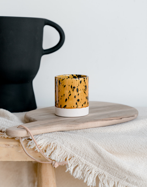 Notre tasse tachetée jaune posée sur une table en bois et une planche en noyer près d'un vase noir