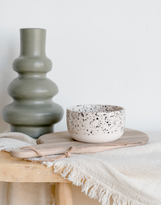 Notre bol arrondis moucheté posé sur une table en bois et une planche en noyer près d'un vase vert d'eau