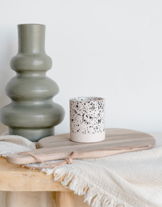 Notre tasse droite mouchetée posé sur une table en bois et une planche en noyer près d'un vase vert d'eau