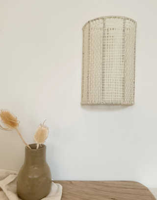 Notre applique en laine accrochée sur le mur près d'un vase en tadelakt couleur taupe et de fleurs séchées